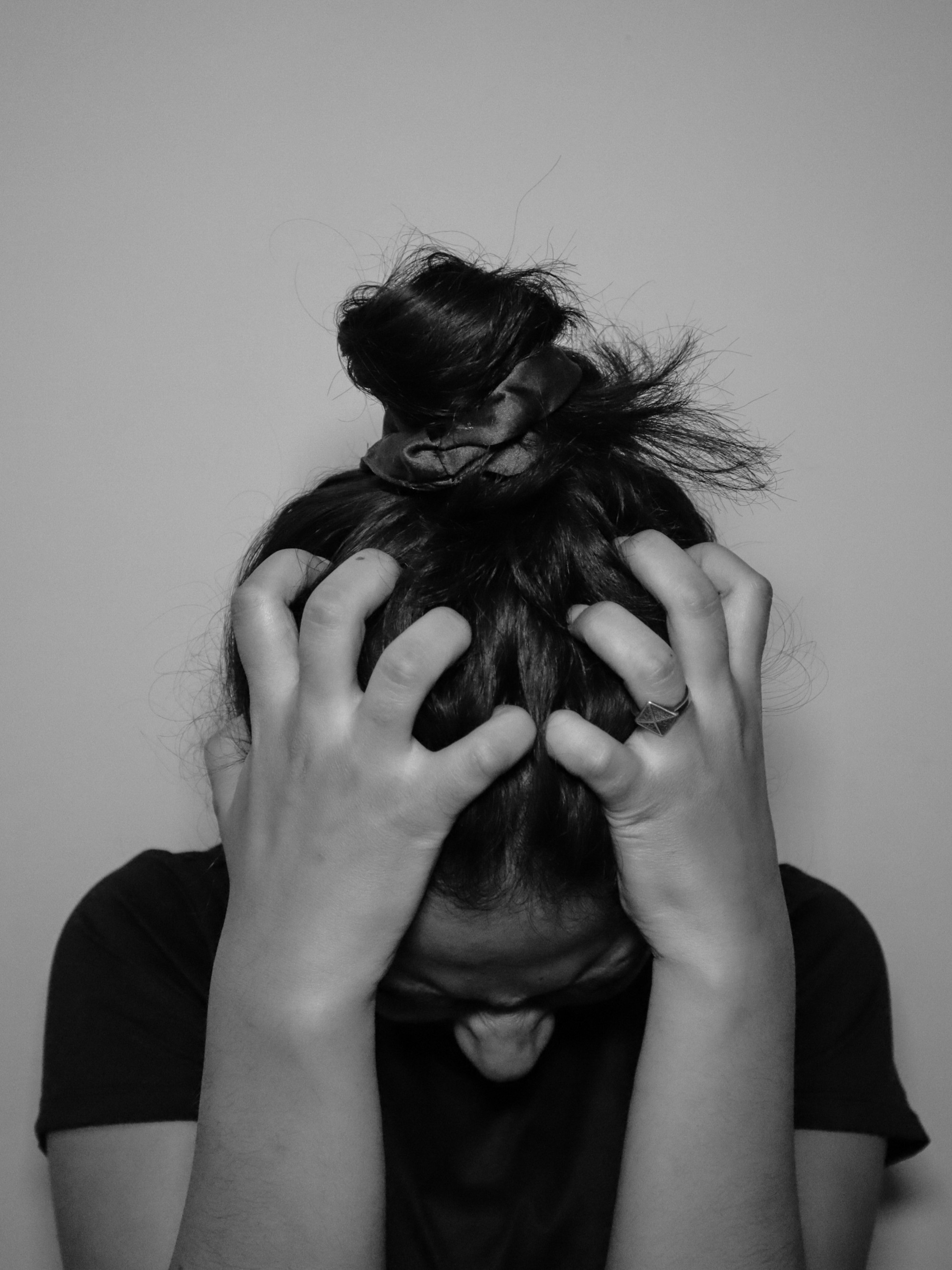 Person with dark hair in a messy bun, hands gripping the head, face obscured by hair and hands.